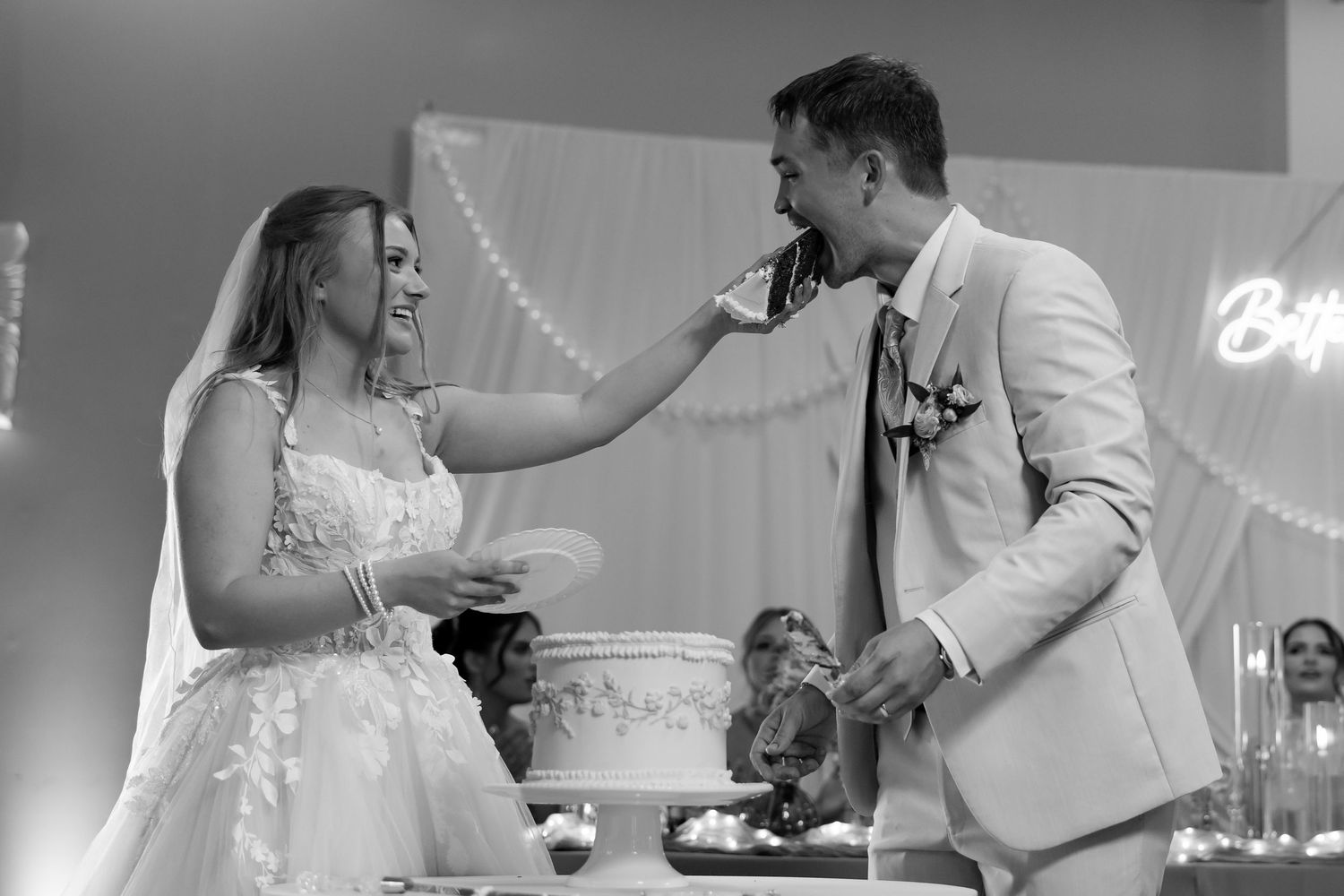 Bride and groom sharing cake cutting moment at wedding reception in black and white.