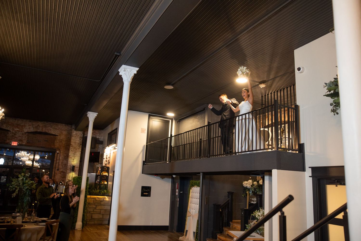 Interior view of a venue with exposed brick walls, columns and mezzanine level balcony.