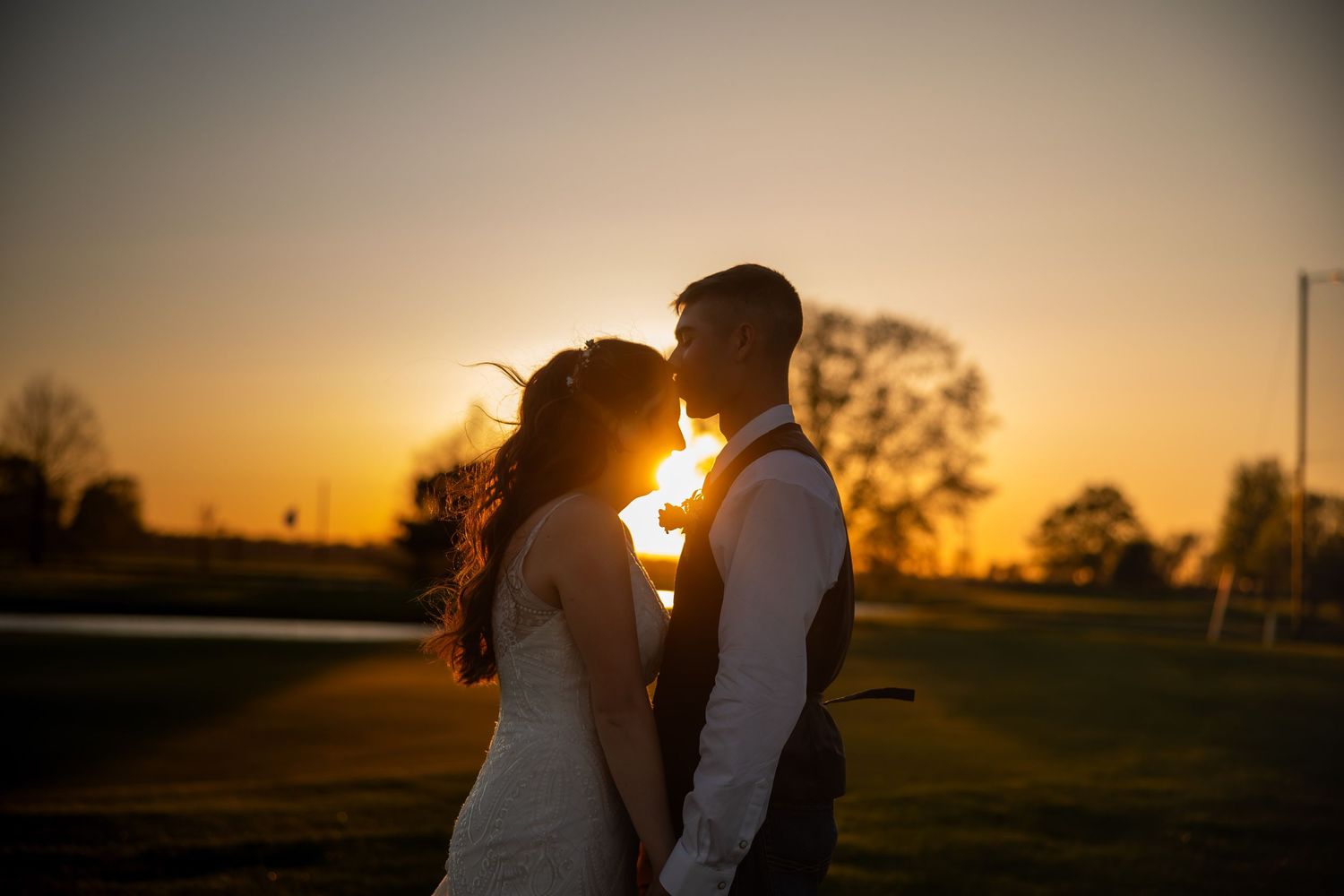 Bride and groom share a romantic sunset silhouette kiss outdoors at golden hour.