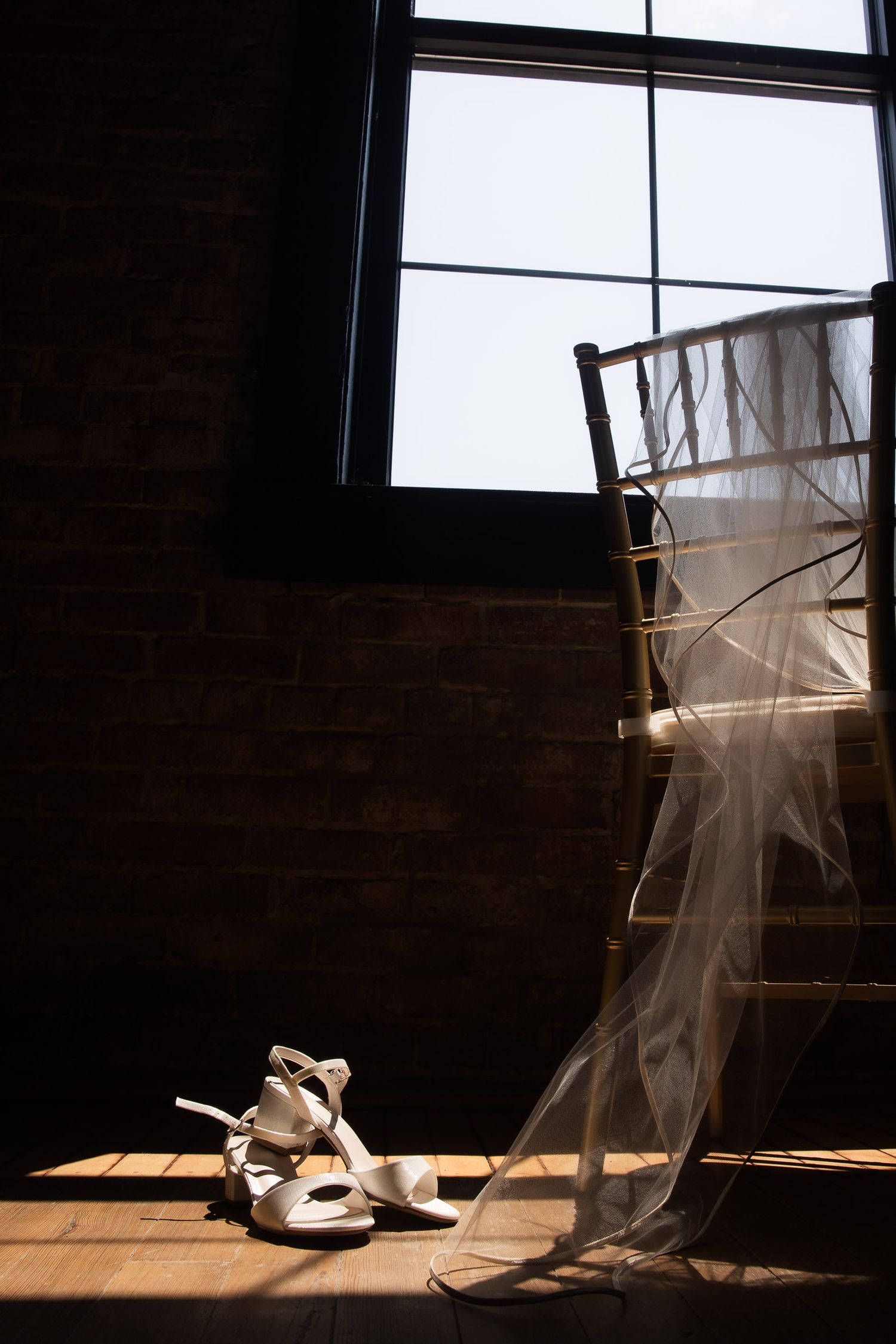 Wedding shoes and veil photographed in dramatic window lighting on wooden floor.
