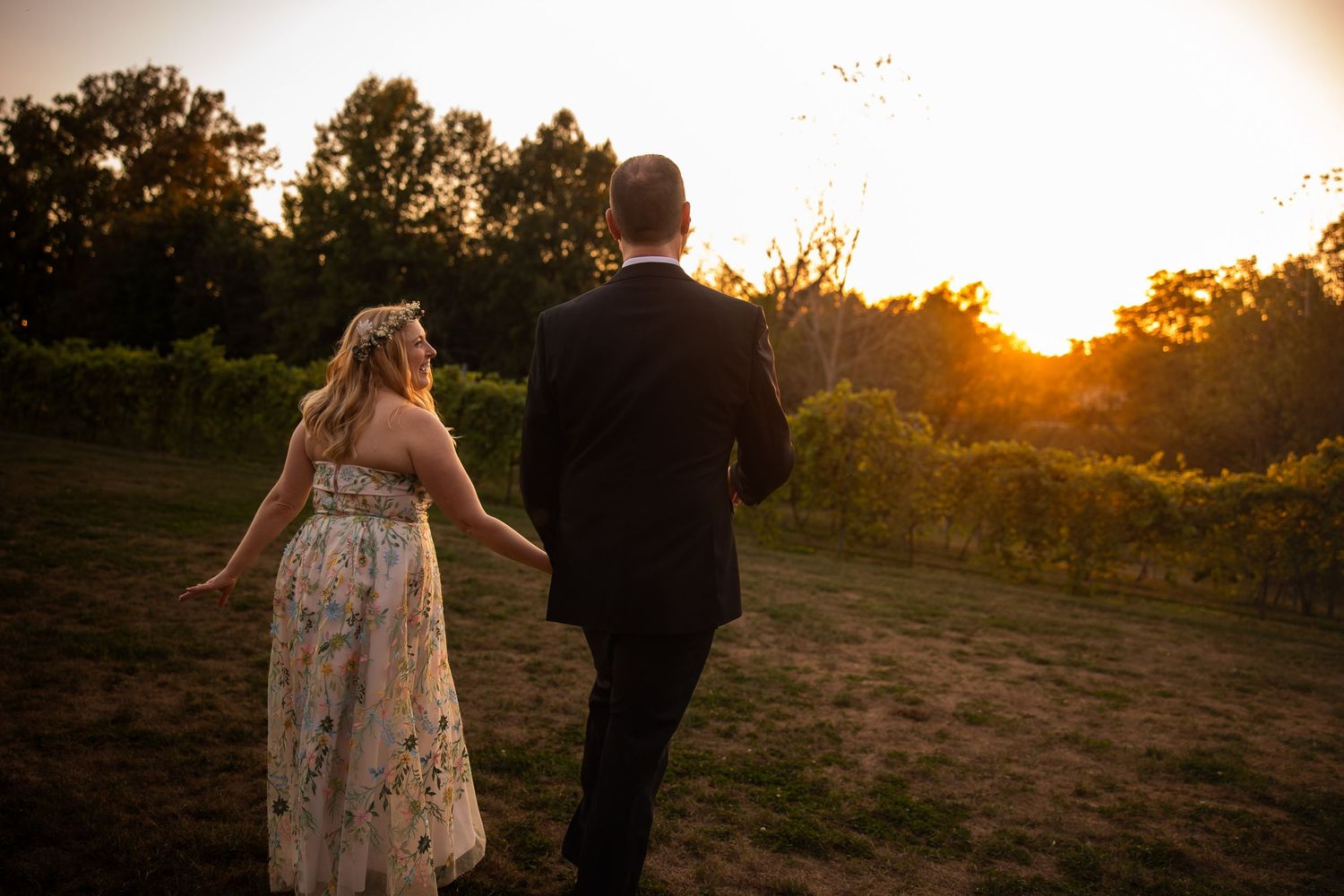 A couple walks together in a field at golden hour as the sun sets behind them.