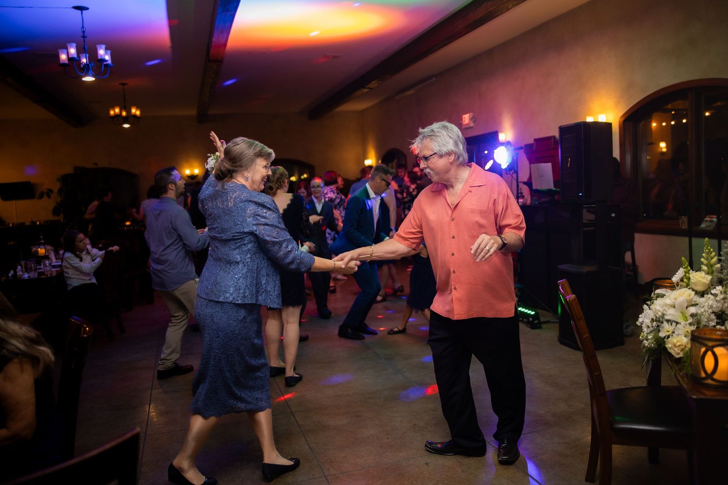 Dancers move across a dimly lit ballroom floor during sunset with colorful ambient lighting creating a warm atmosphere.