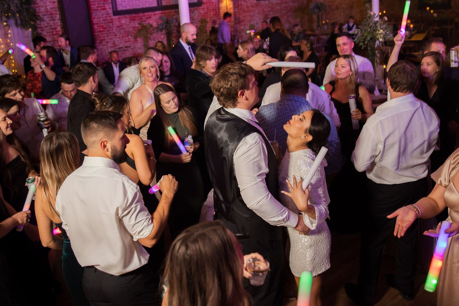 Energetic wedding reception dance party with guests in formal attire under purple lighting.