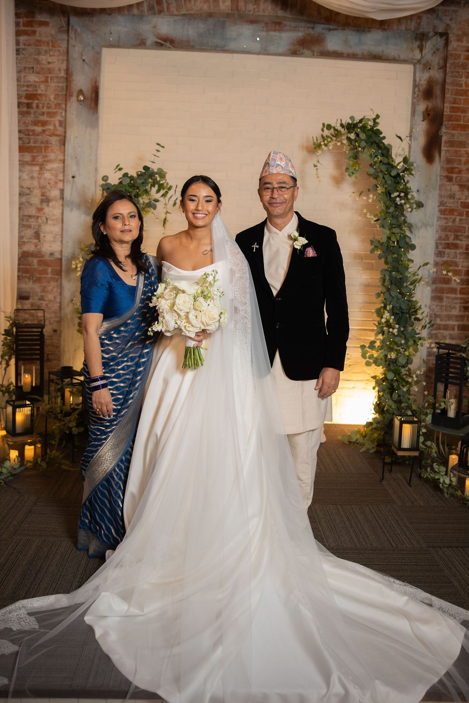 A wedding portrait in front of a decorated arch with lanterns and greenery.