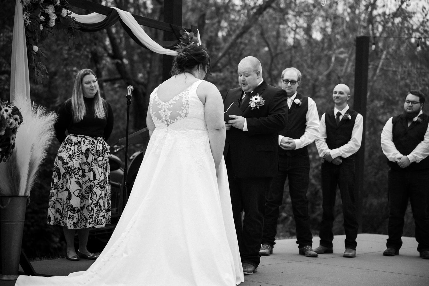 A black and white photograph captures a wedding ceremony in progress with guests watching from the sides.