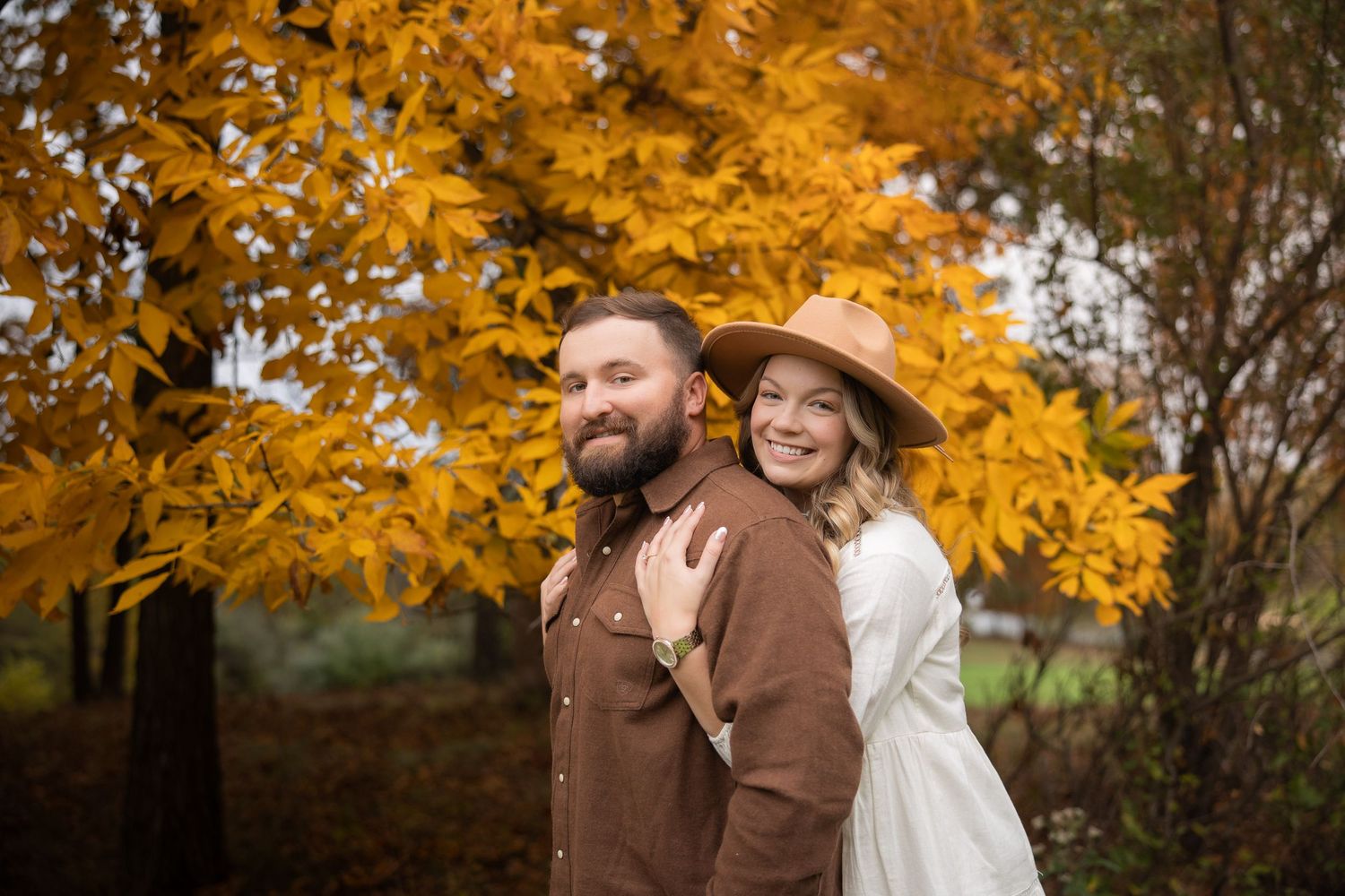 A couple embraces outdoors surrounded by vibrant golden autumn foliage during a fall photoshoot.