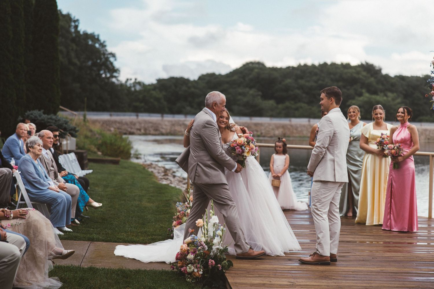 Bride and groom exchange vows at outdoor waterfront wedding ceremony with bridesmaids and seated guests.