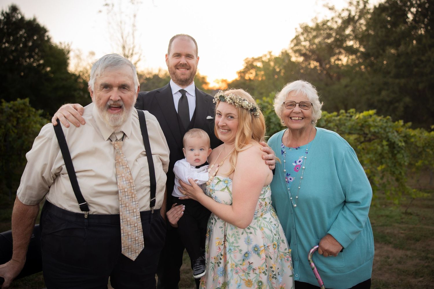 Family members gather for photos in front of vineyard at sunset.