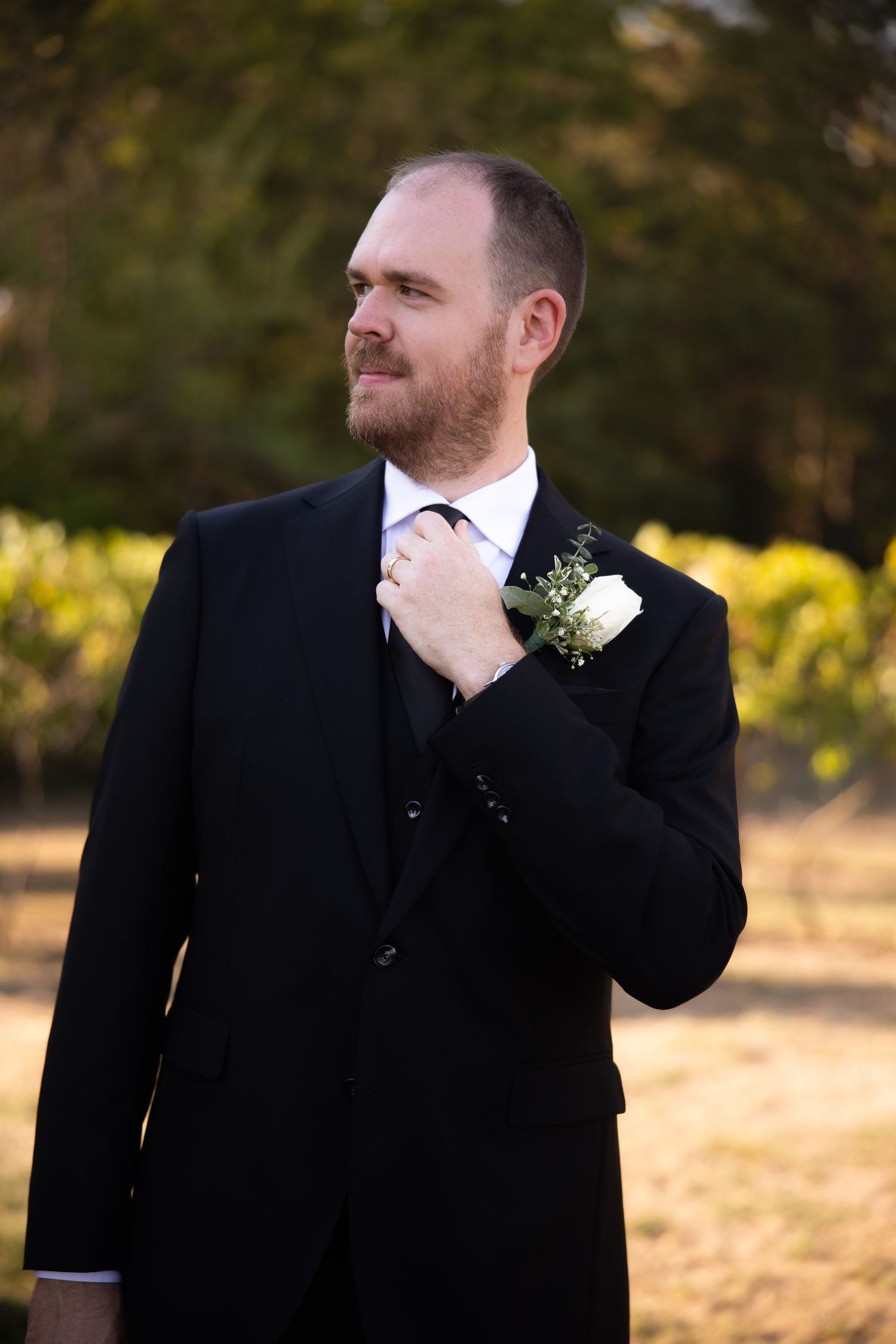 A person in a black suit adjusts their tie while standing outdoors.