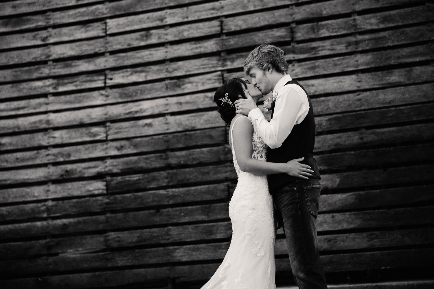 Wedding couple poses against rustic wooden wall background in black and white.