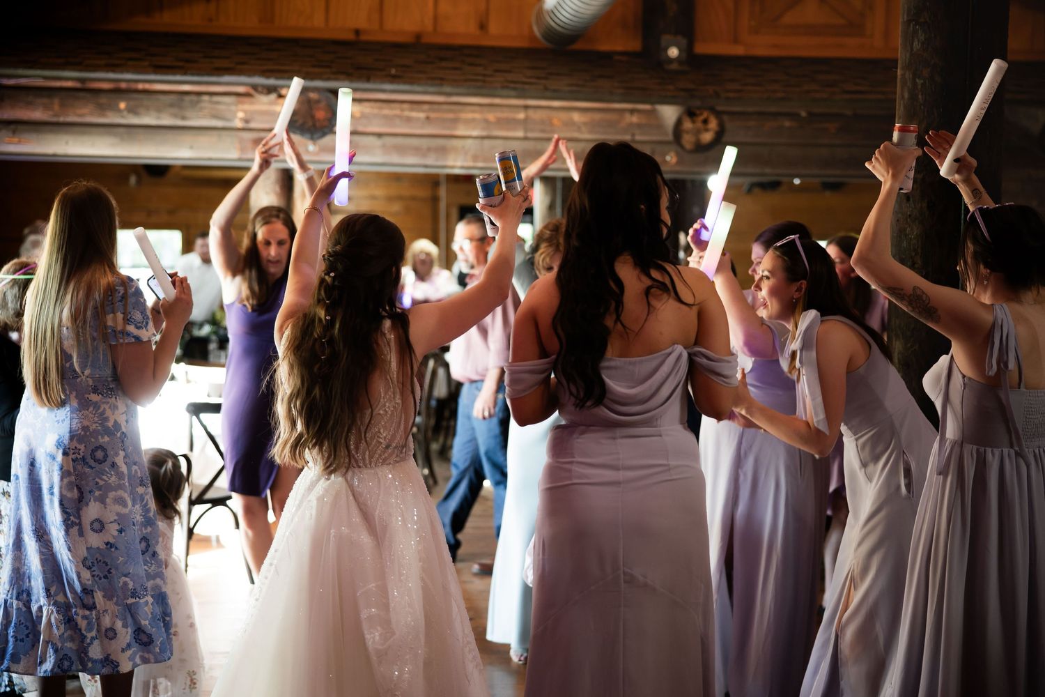 Bridesmaids in purple dresses celebrating with bride on dance floor at rustic barn wedding reception.