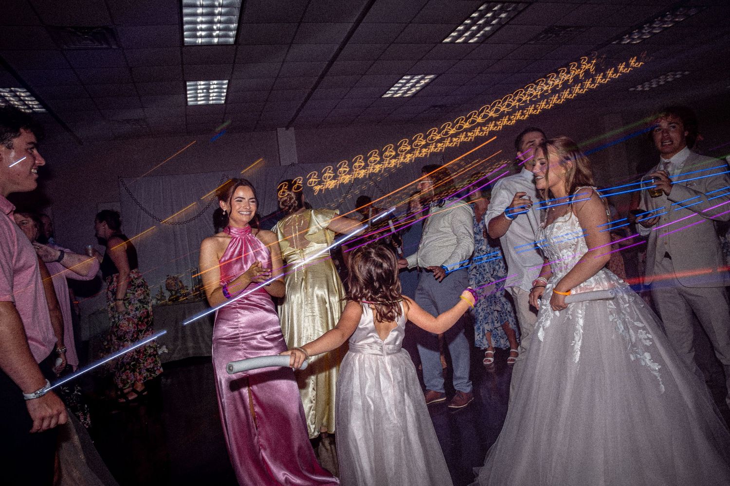 Bride and guests dancing with colorful light sticks at wedding reception party.