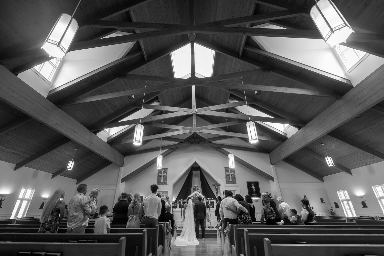 Black and white photo of a wedding ceremony inside a church with vaulted ceilings and guests seated in wooden pews.