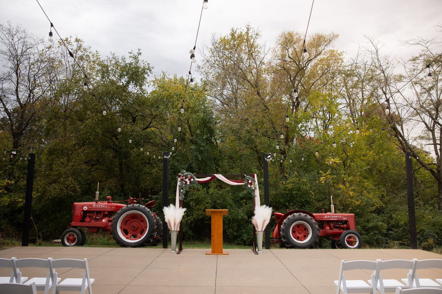 A panoramic view shows tractors and farm equipment arranged in a line along a tree-lined path during autumn.