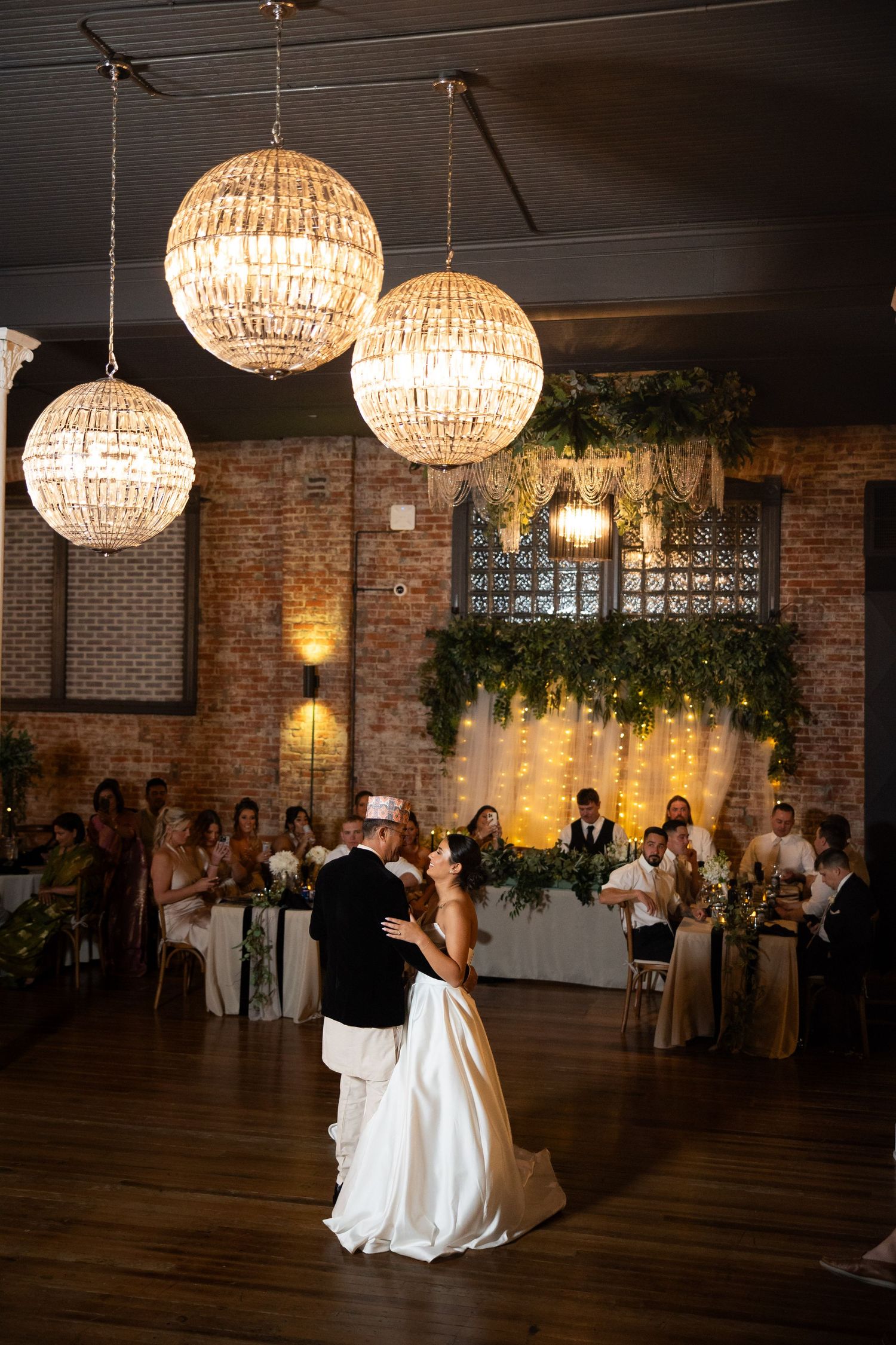 A couple shares their first dance under crystal chandeliers in an elegant brick-walled reception venue.