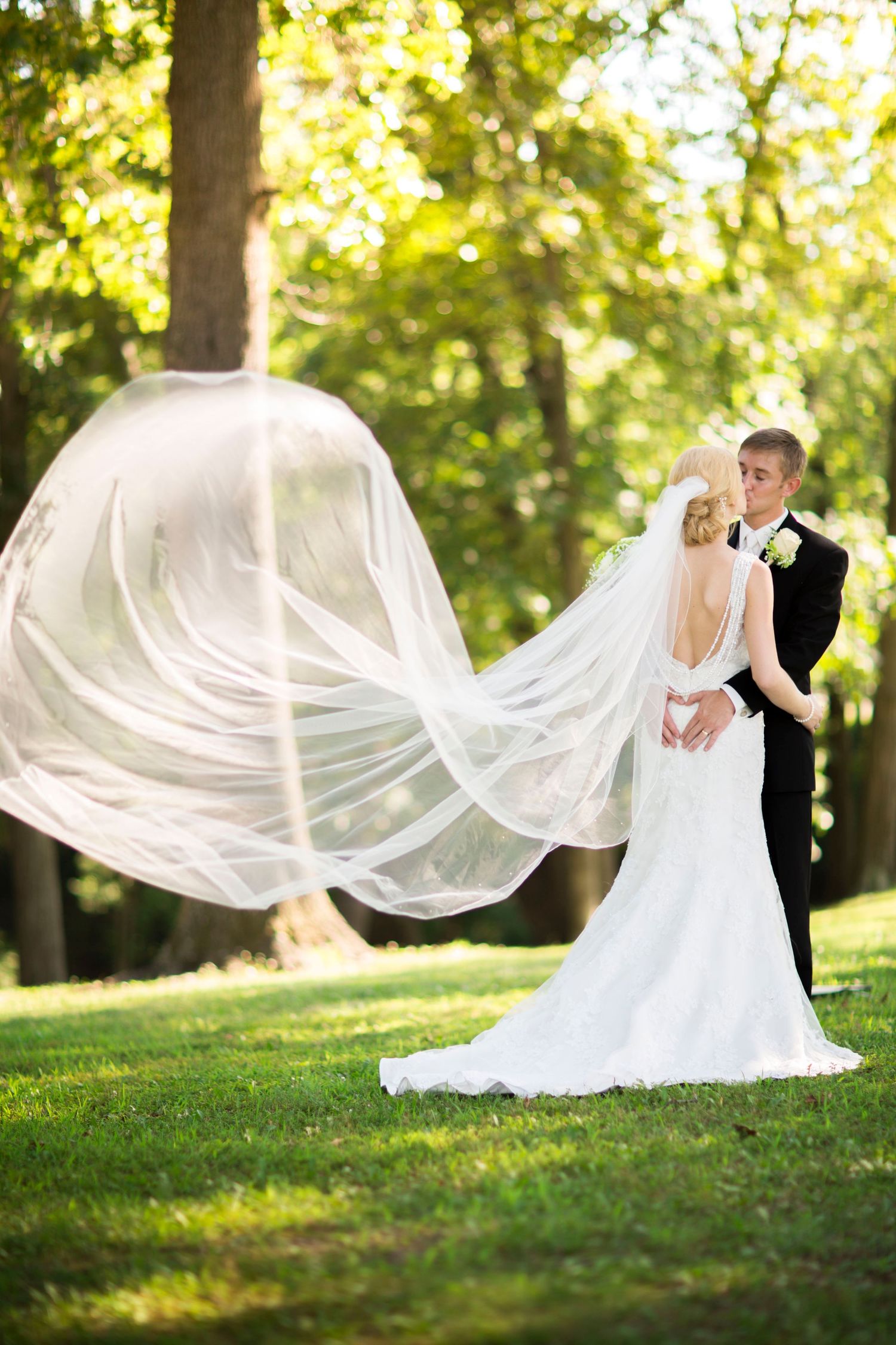 White wedding veil flows dramatically in sunlit garden setting.