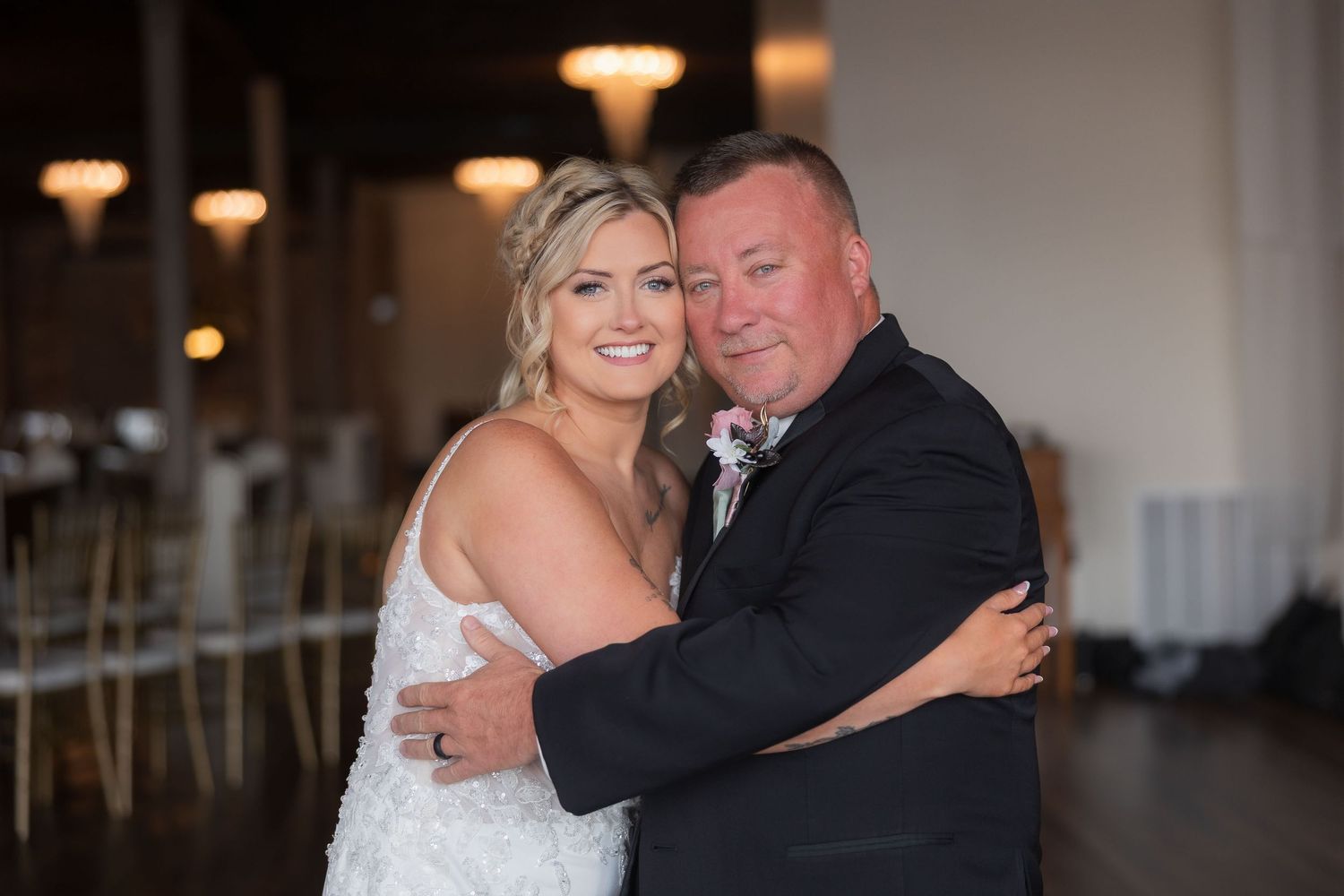 A wedding couple shares an intimate moment in front of a rustic brick wall with floral decorations.