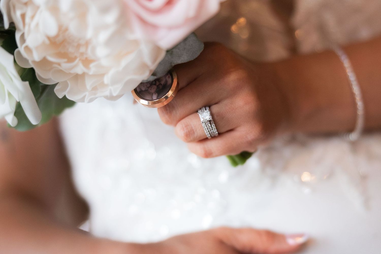 A hand wearing a white wedding ring holds a delicate pink rose bouquet in soft natural lighting.