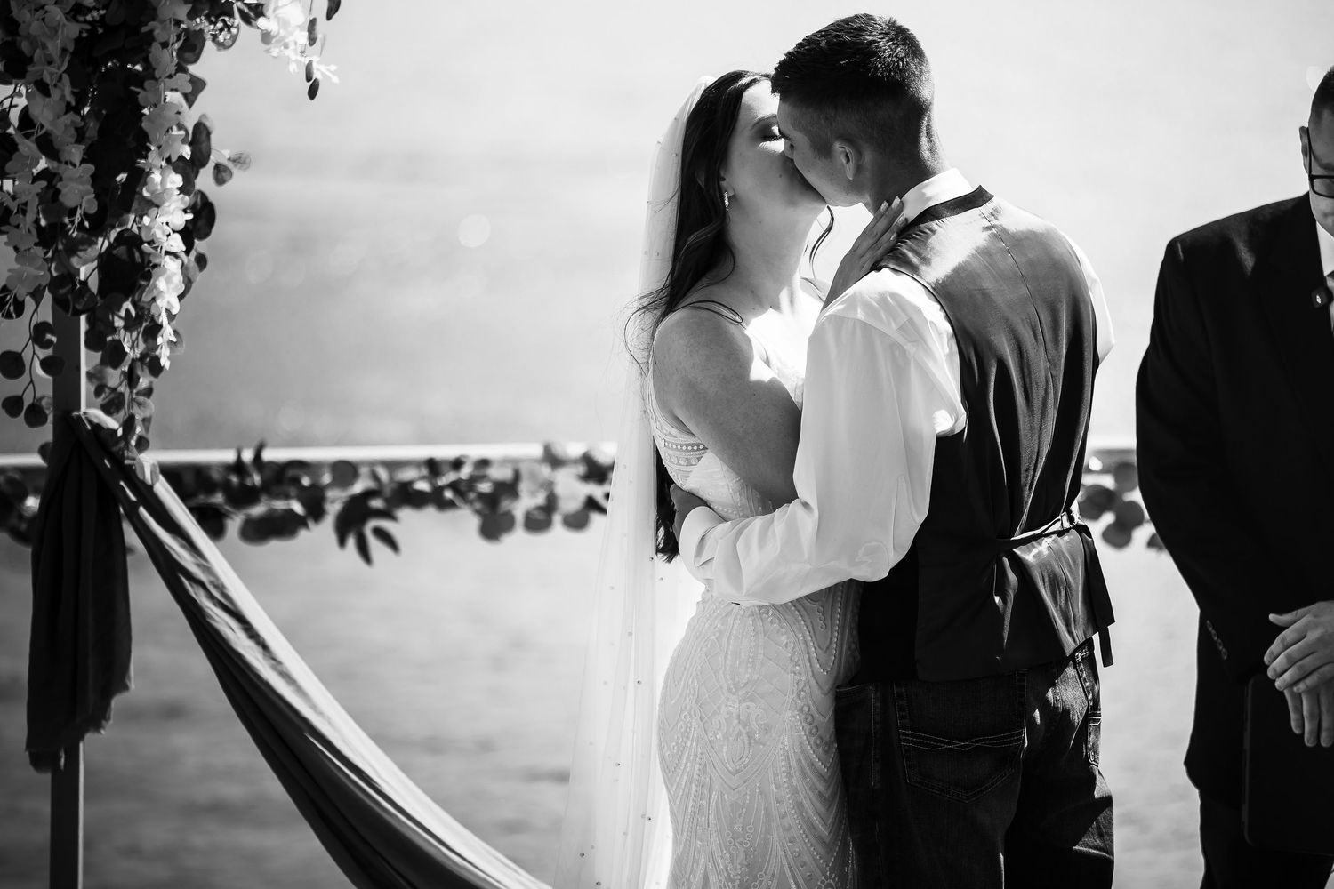 Black and white photo of bride and groom sharing first kiss at outdoor beach wedding ceremony.