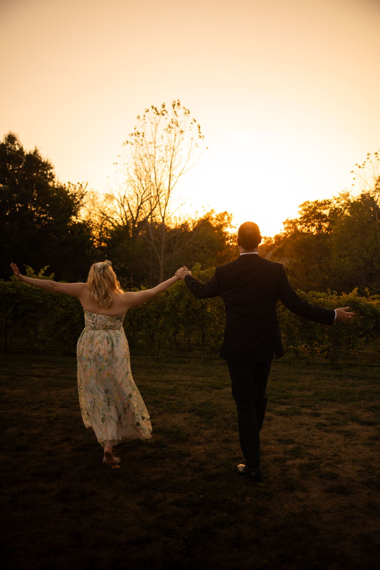 A couple walks hand in hand across a field during golden hour sunset.