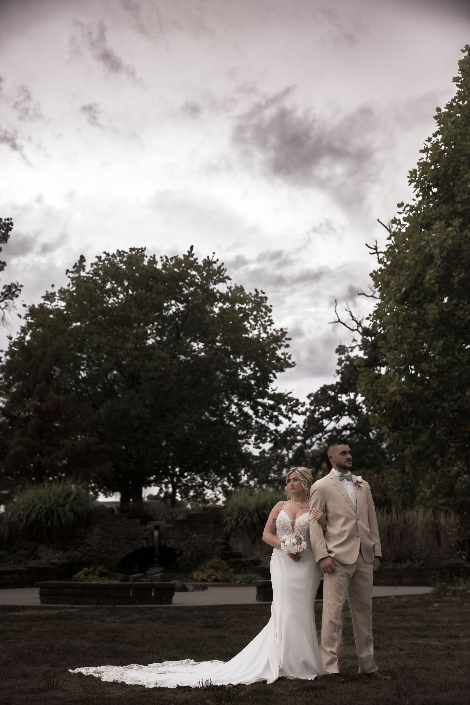 Dramatic sunset wedding portrait with cloudy skies and trees in the background.