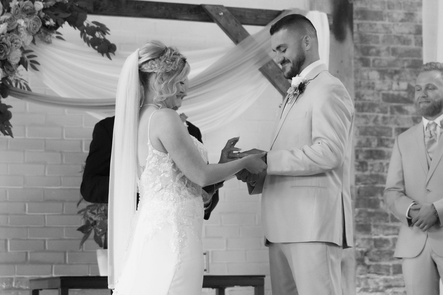 Bride and groom share tender moments during their wedding ceremony under a white draped arch.