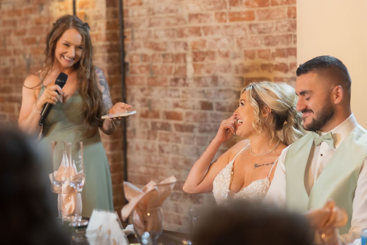 Wedding reception candid moments showing guests laughing and celebrating against brick wall backdrop.