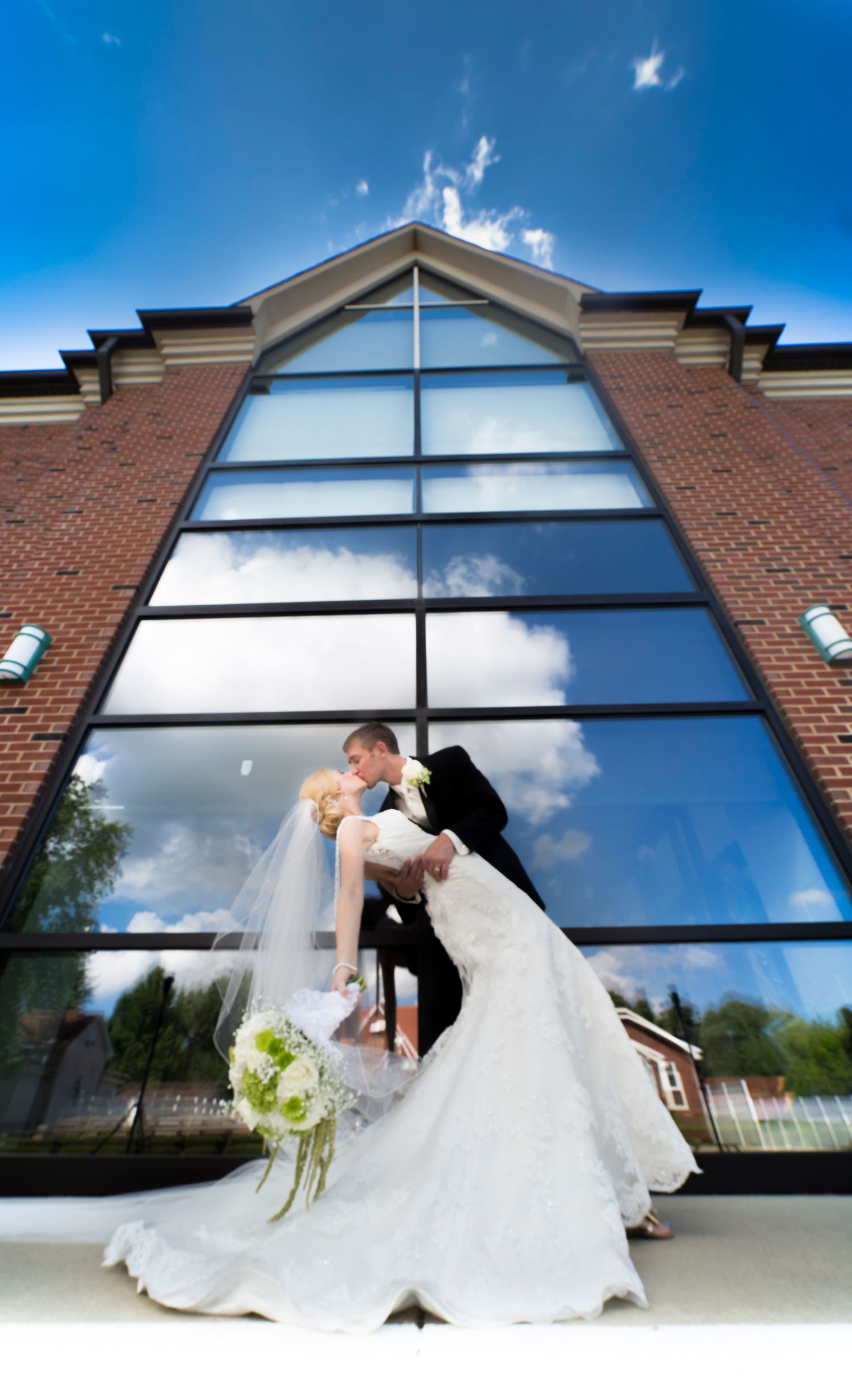 Artistic wedding photo sequence against modern building with large reflective windows and blue sky.