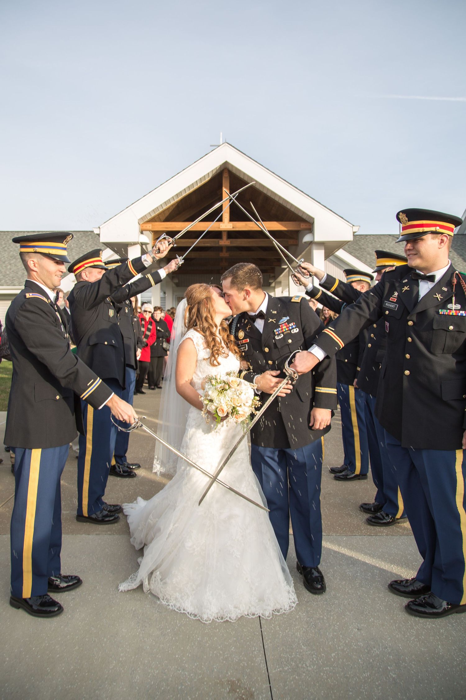 Military service members form an honor guard with raised swords as newlyweds pass beneath during a wedding ceremony.