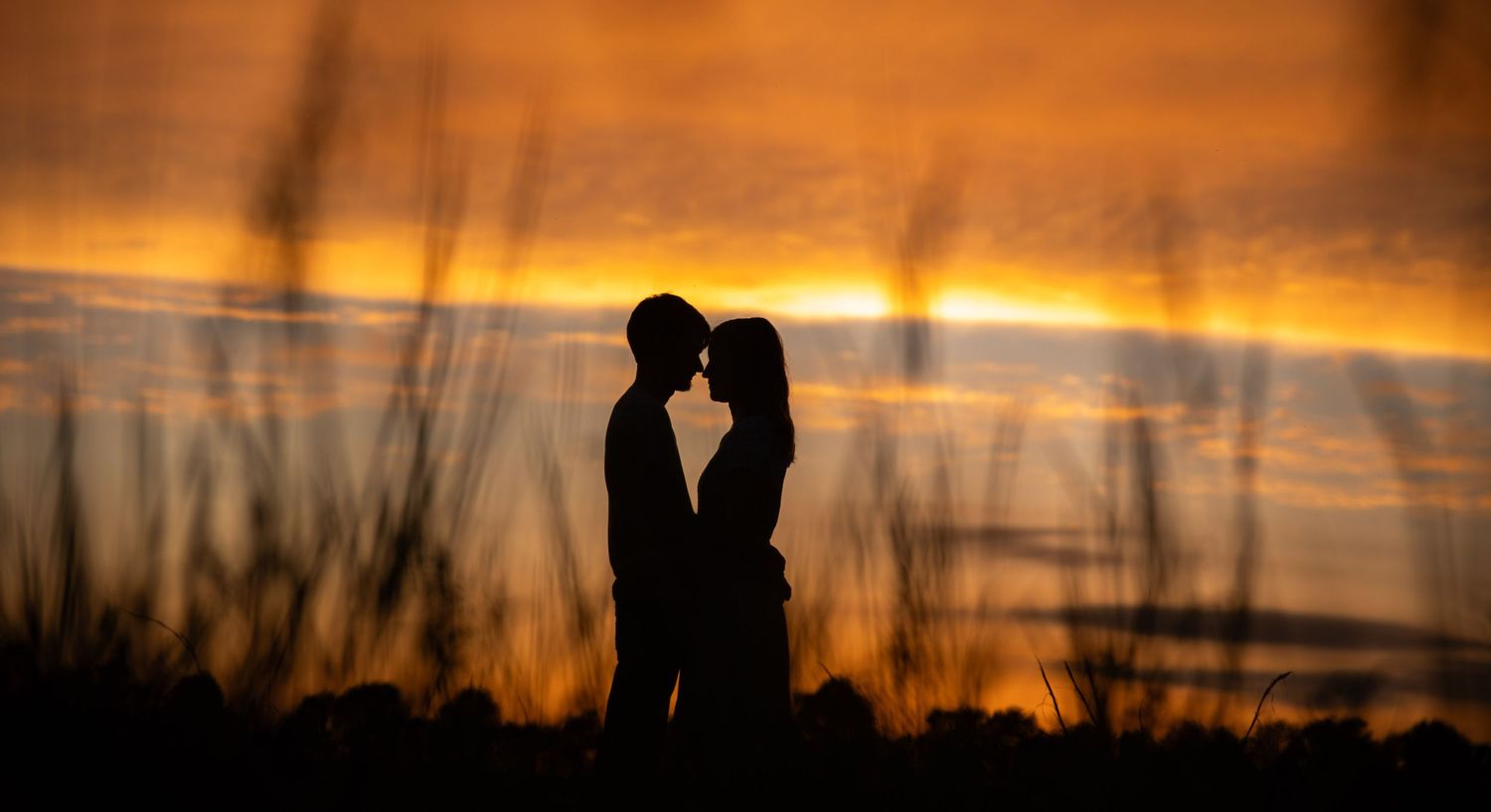 Romantic silhouettes of a couple embracing against a dramatic orange and purple sunset sky.