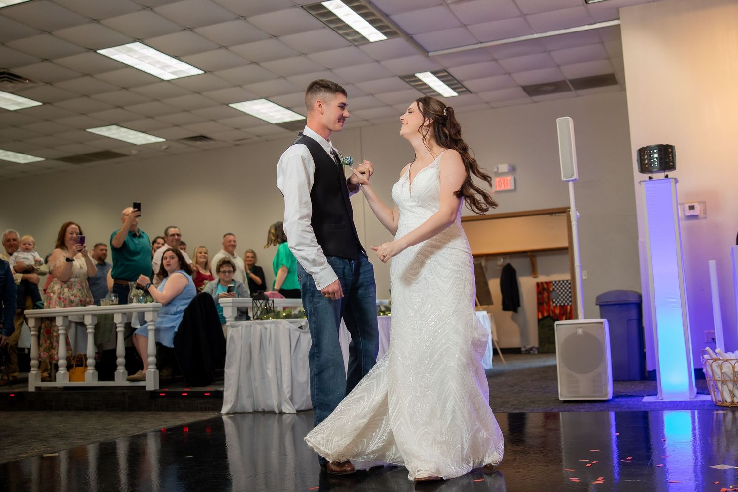 Bride and groom share their first dance together on the dance floor surrounded by wedding guests.