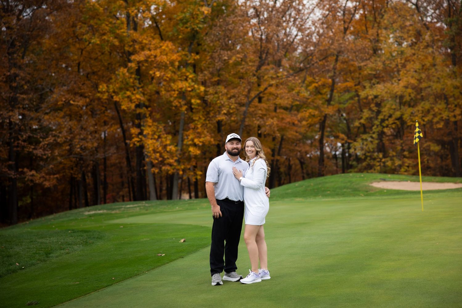 Golfers enjoy a round on a scenic autumn golf course with vibrant orange foliage in the background.