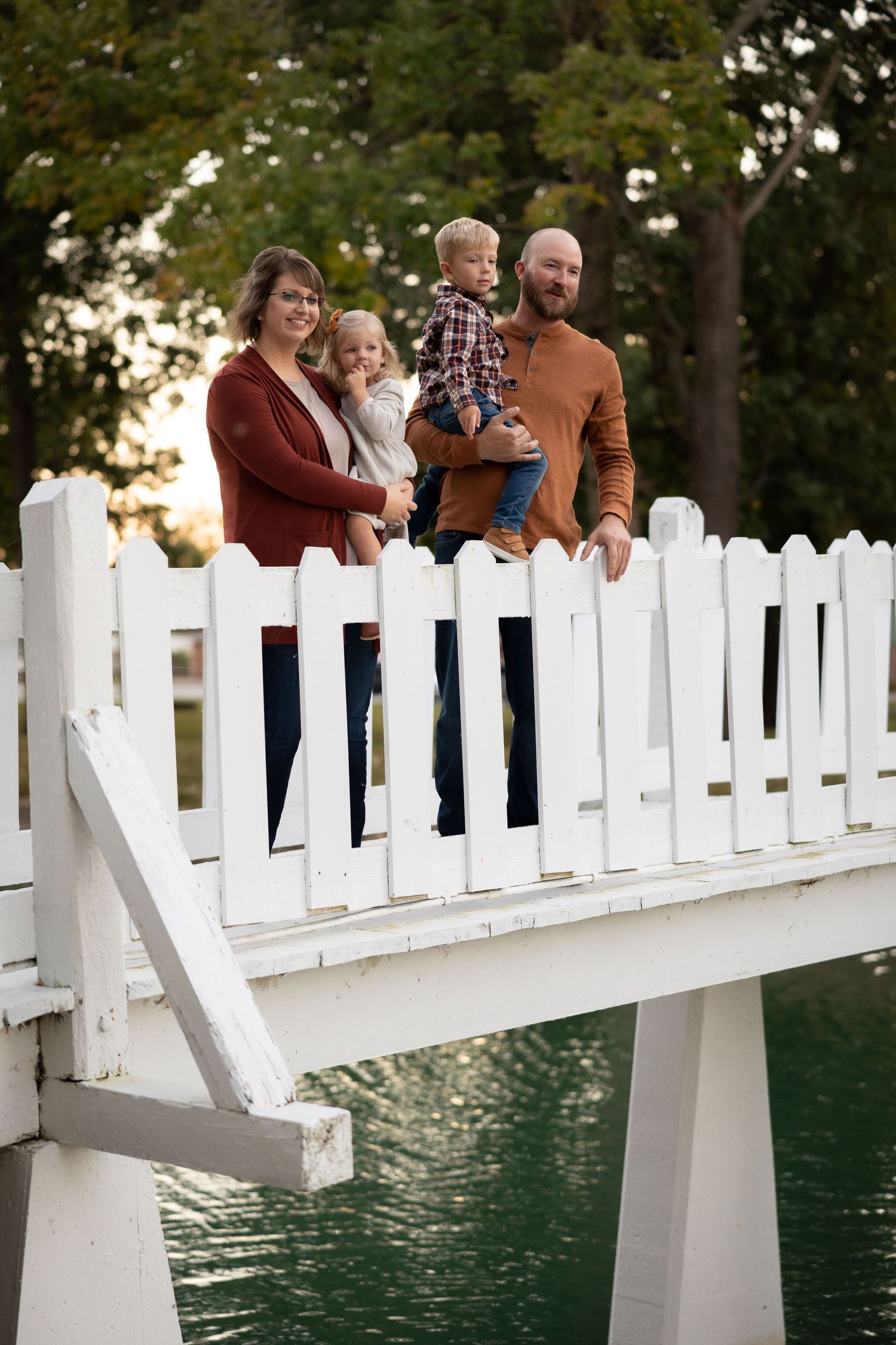 Family leaning against white picket fence overlooking water at sunset.