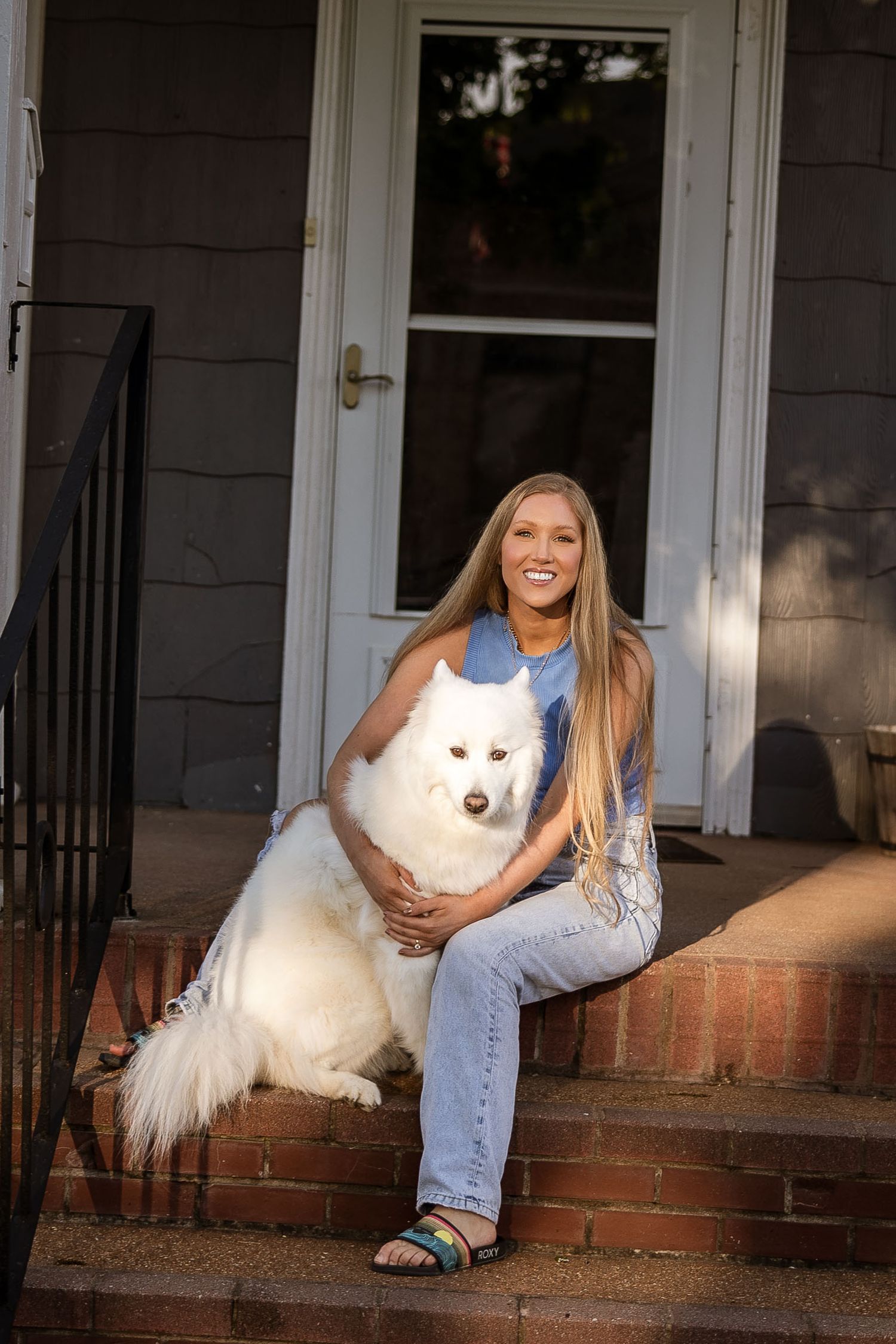 A fluffy white dog and owner share playful moments on a front porch during a casual photoshoot.