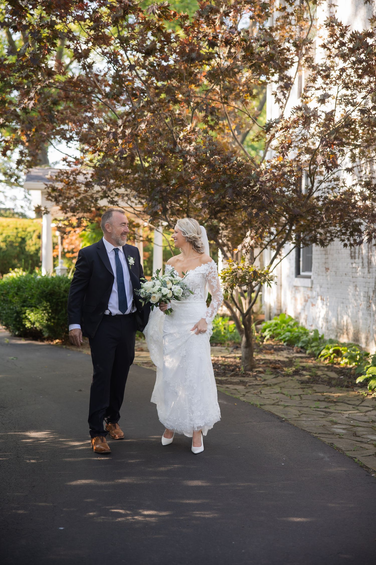 Wedding couple walking along a stone path surrounded by autumn trees.