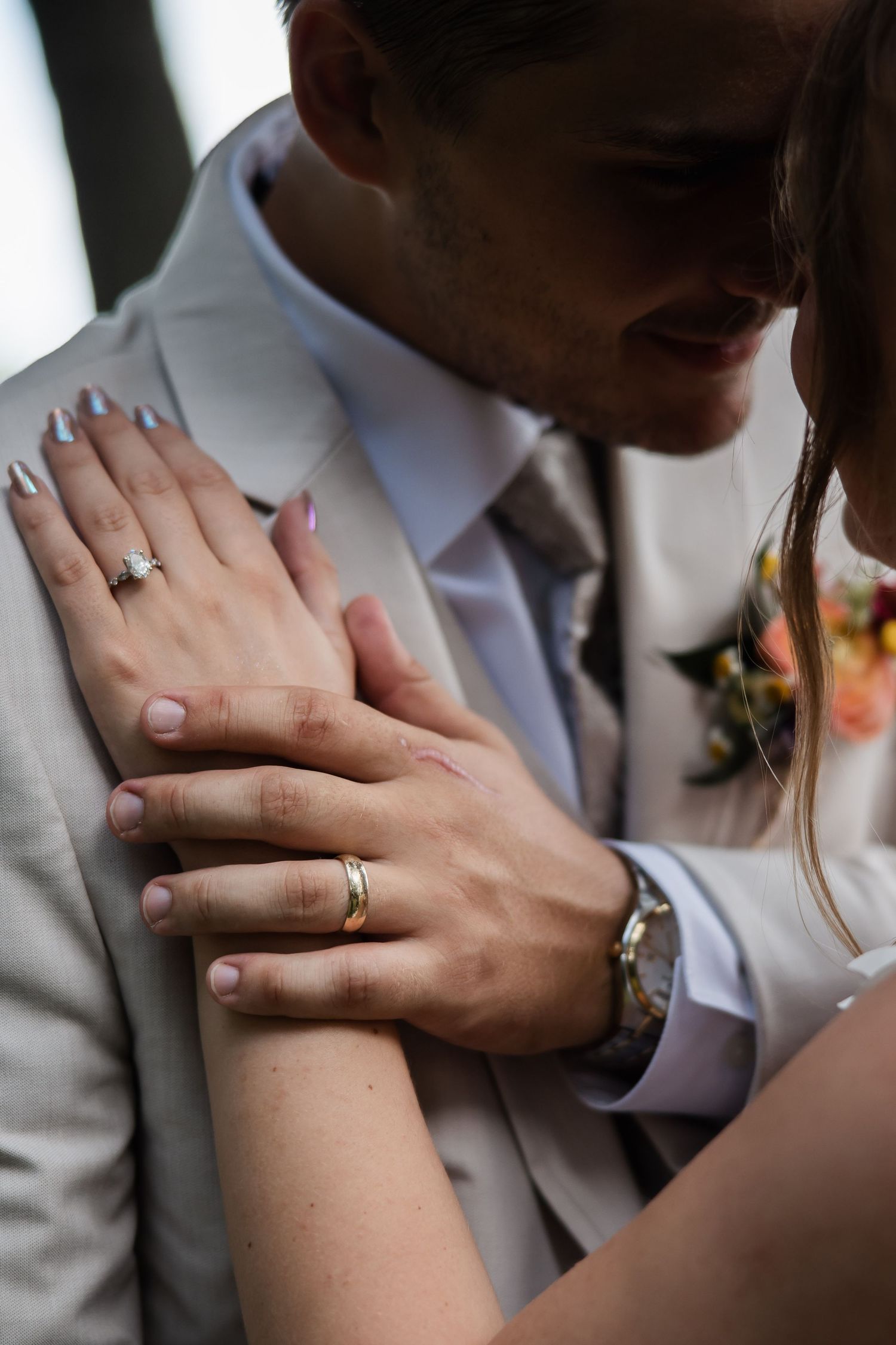 Close-up of bride and groom hands showing diamond engagement ring and gold wedding band.