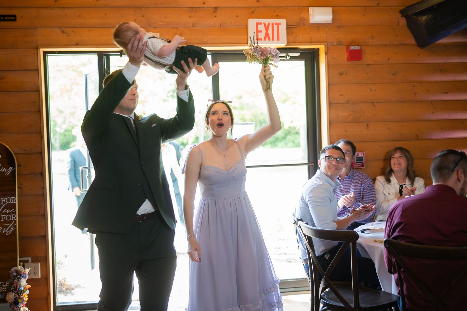 Excited bridesmaid in lavender dress catches bouquet toss at lively indoor wedding reception.