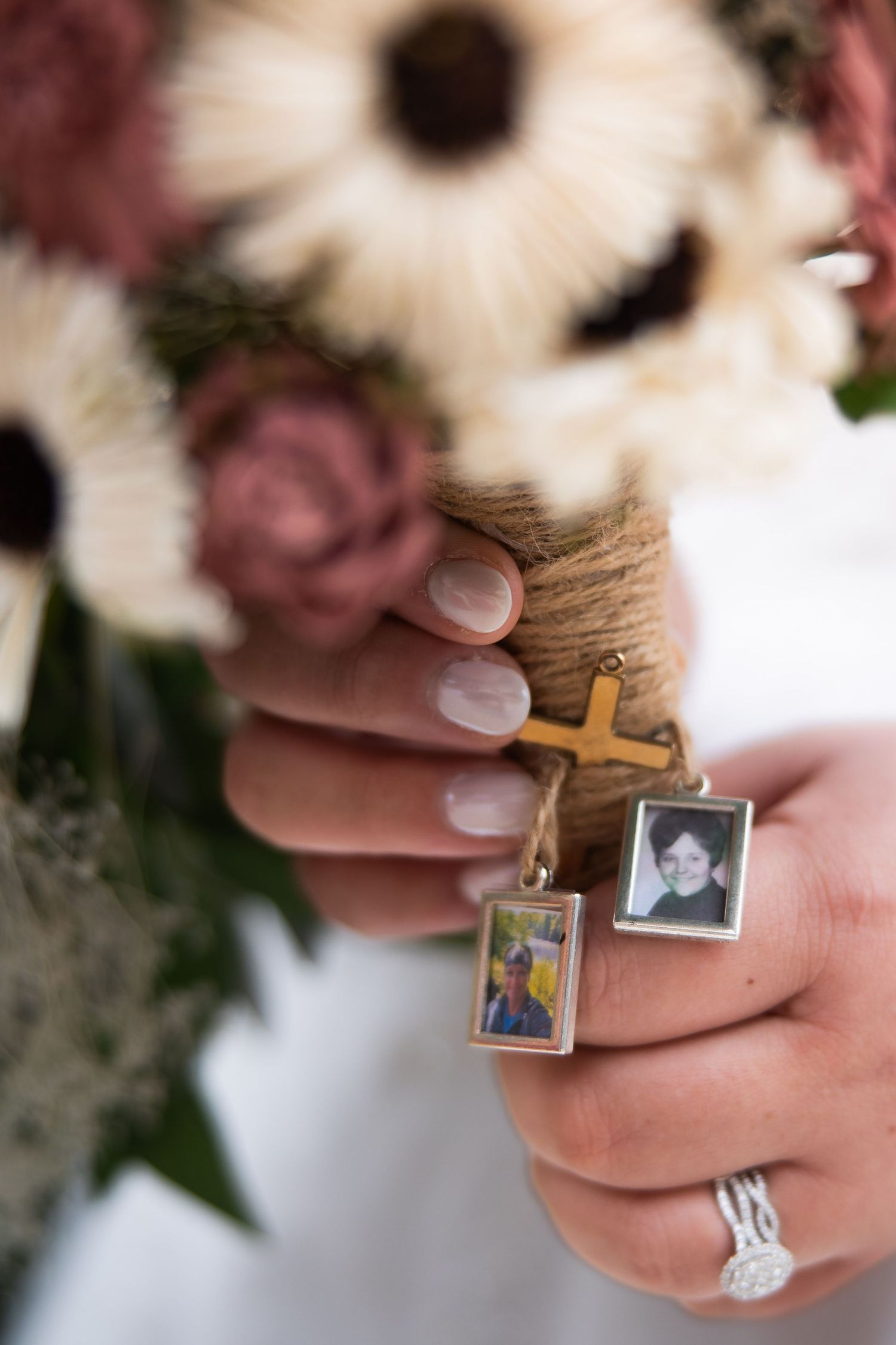 Hands holding a rosary with small photo charms and a cross pendant against a blurred floral background.