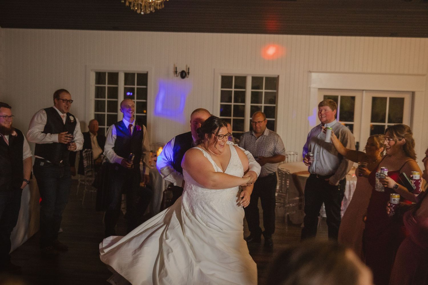 Couples dancing on a hardwood floor at an elegant wedding reception under warm lighting and chandeliers.