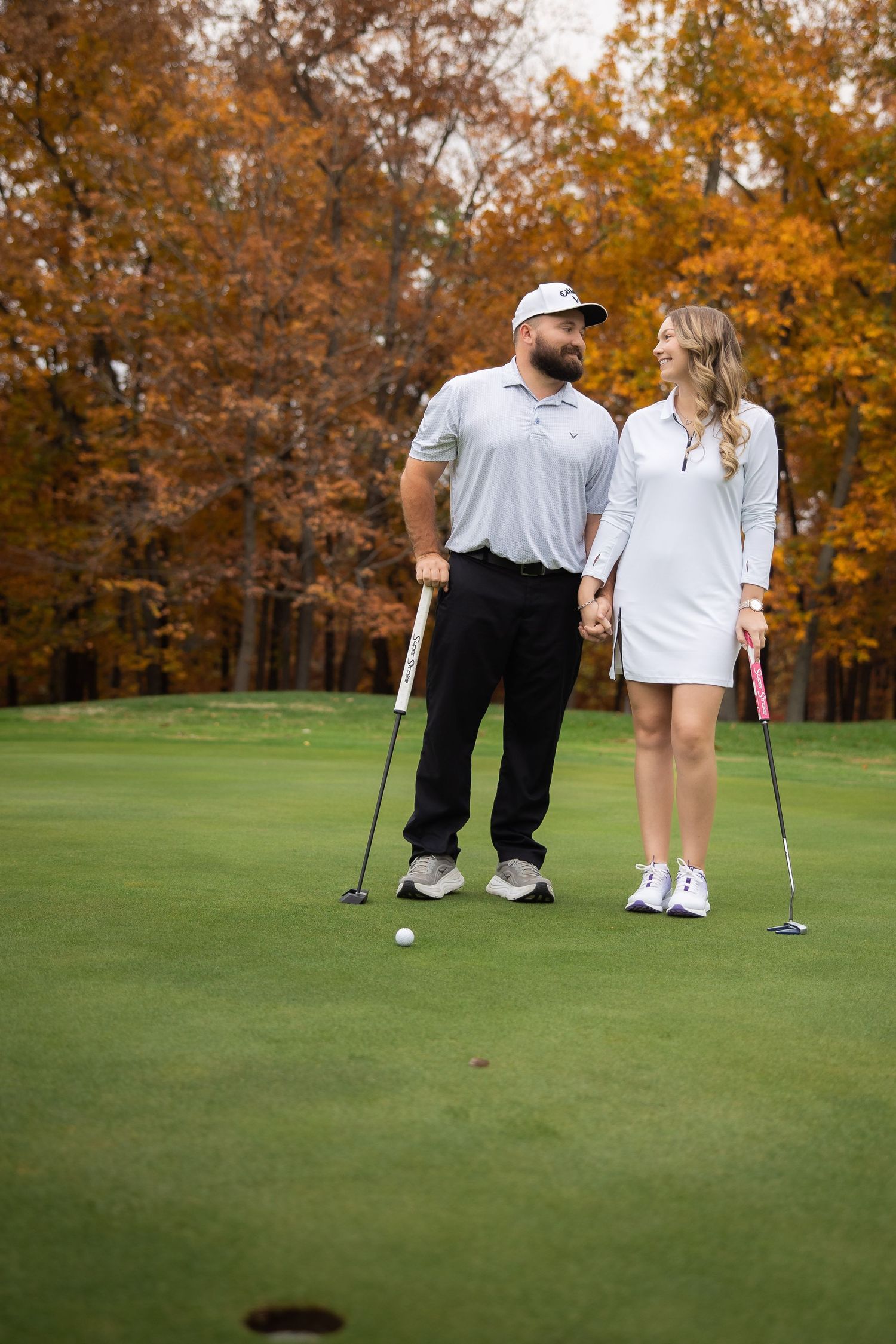 Two golfers standing on a putting green with autumn foliage in the background during a round of golf.