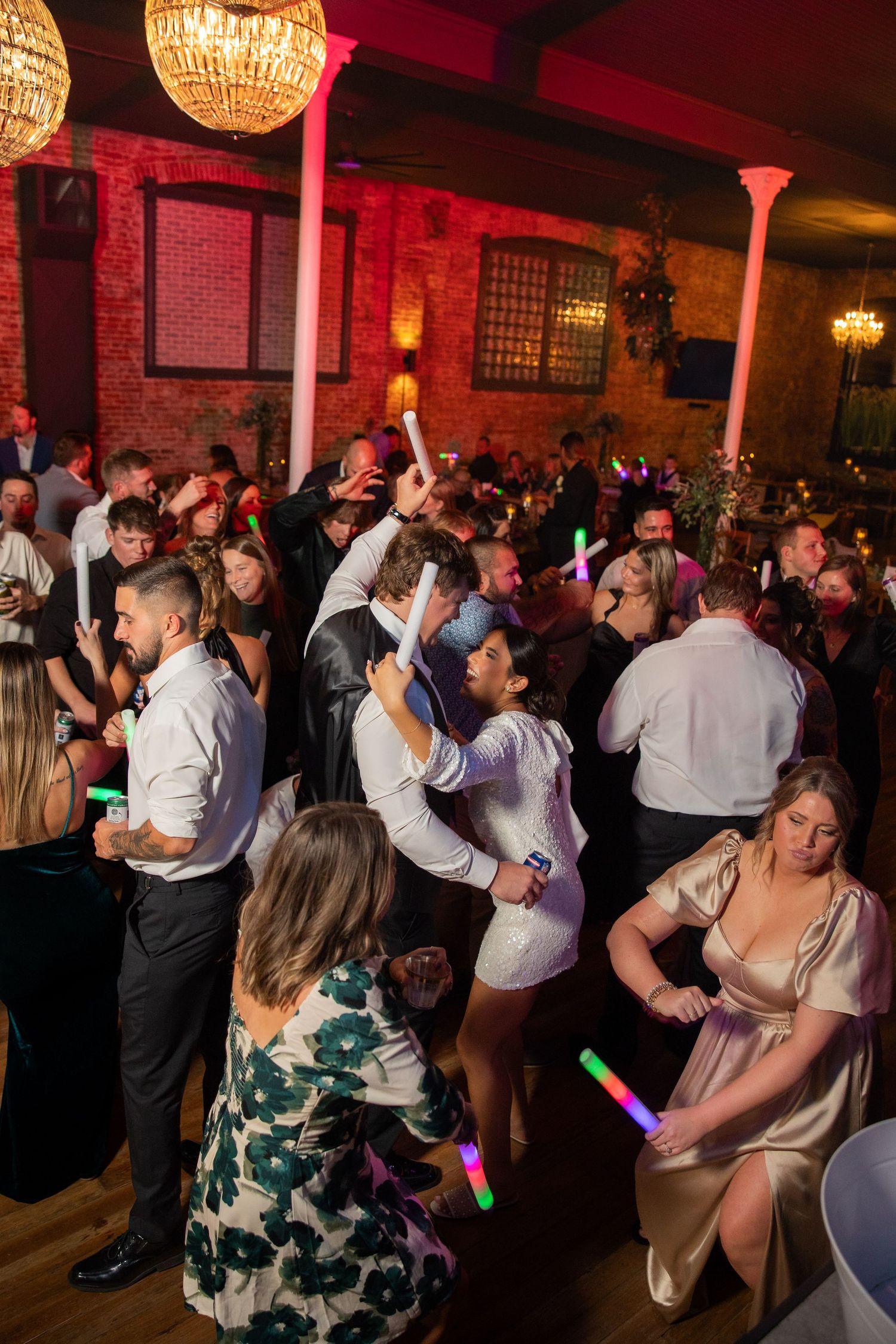 Wedding guests dancing and celebrating on a dimly lit dance floor with glowing red ambient lighting.