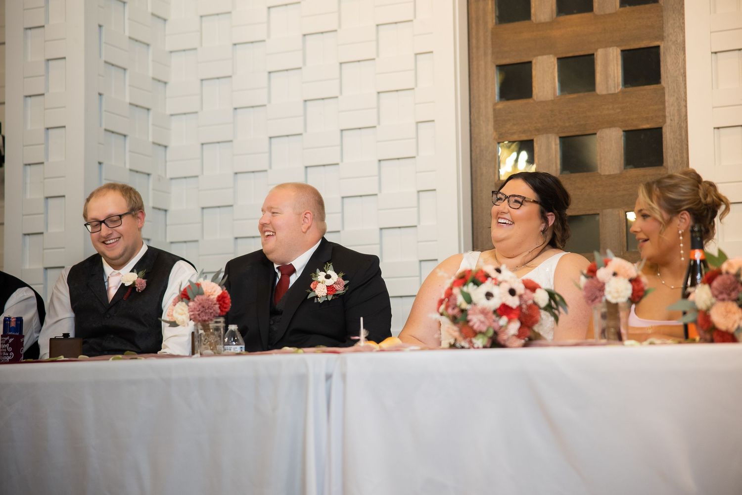 Wedding guests seated at long tables during reception with decorative white wall panels in background.