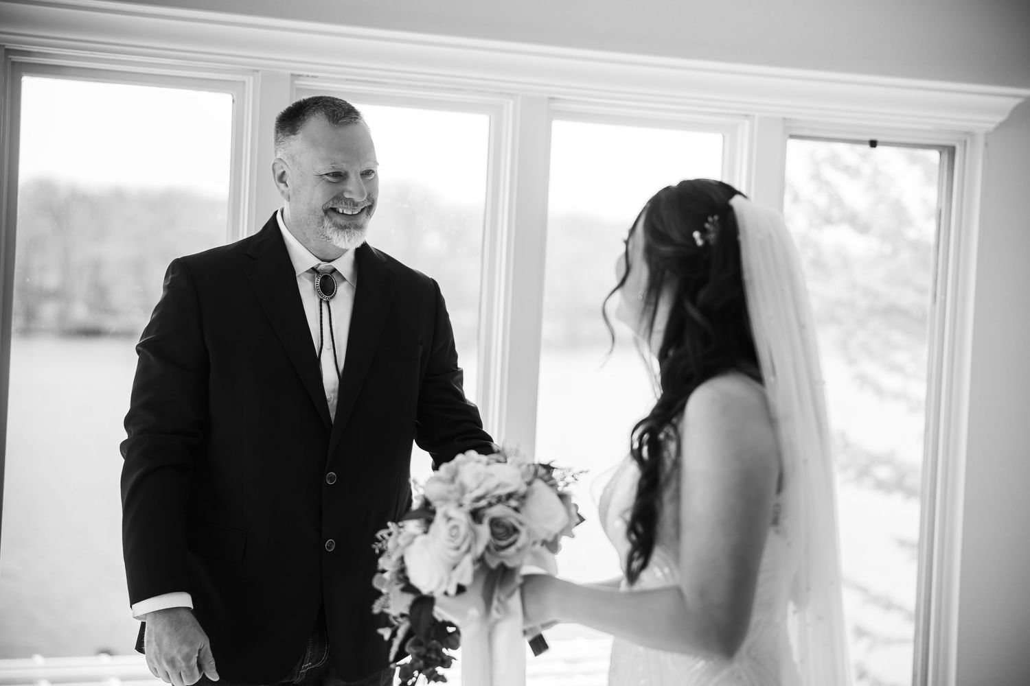 Black and white photo of a smiling groom seeing his bride for the first time at their wedding.