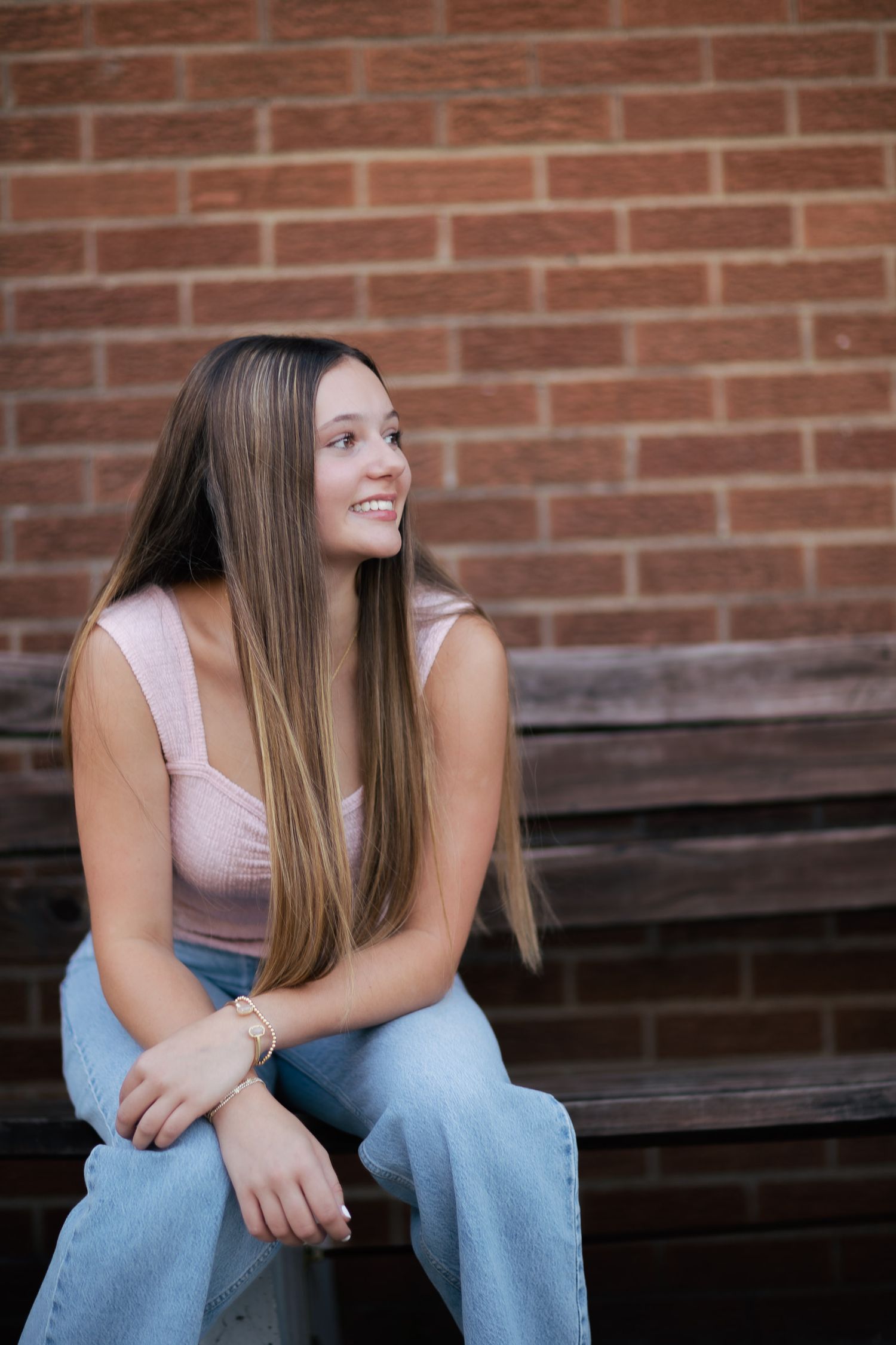 Casual portrait session against a brick wall background wearing jeans and pink top.