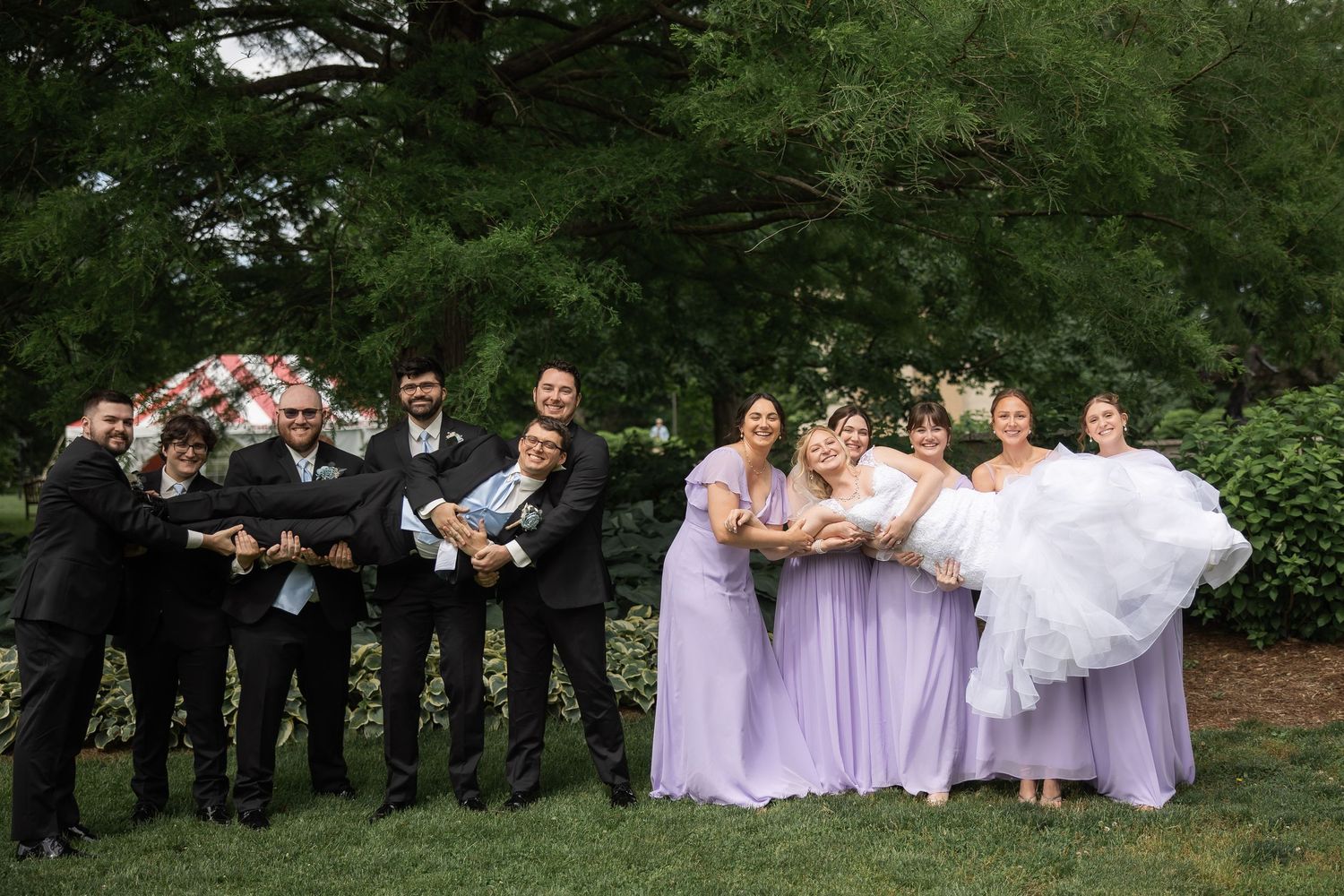 Wedding party poses for fun group photos outdoors in a lush green garden setting.