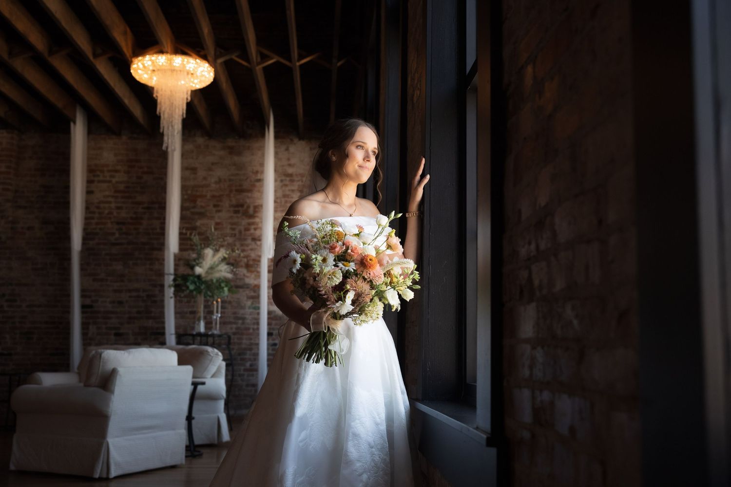 Elegant bridal portrait in a rustic venue with dramatic lighting and white gown.
