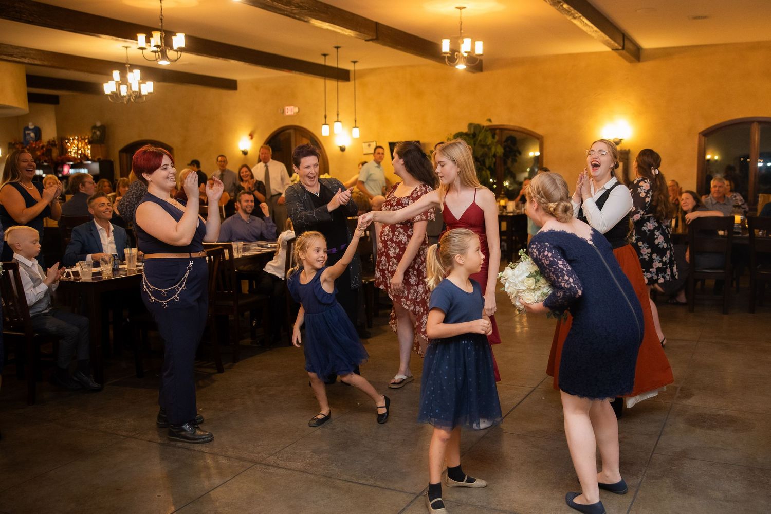 Wedding guests dancing and celebrating on the dance floor at an indoor reception venue.