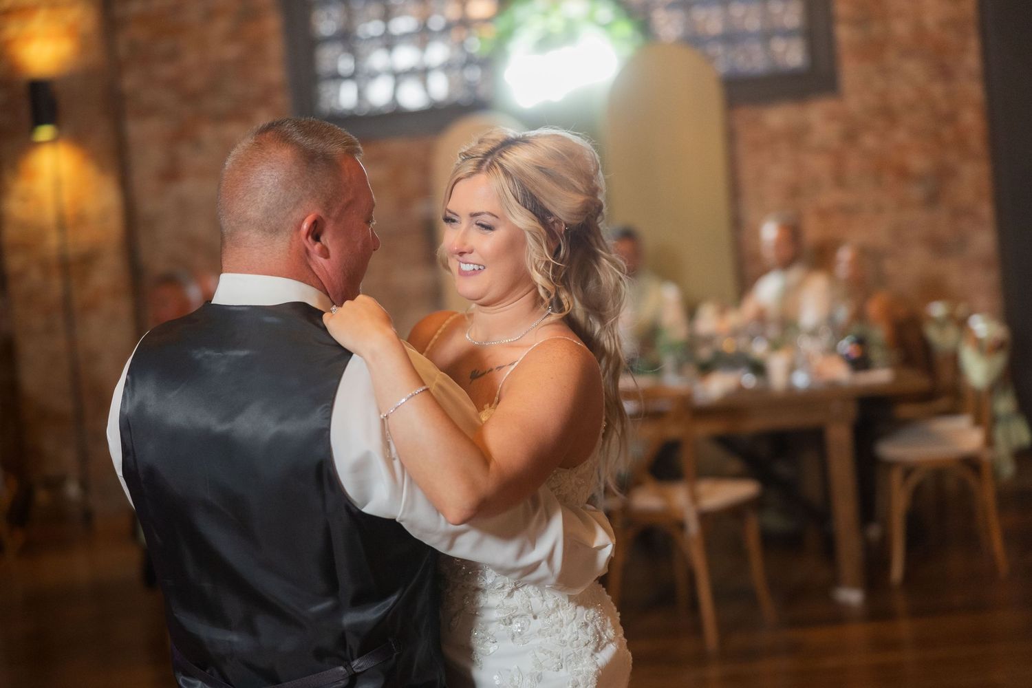 Romantic dance moments at wedding reception with rustic brick wall backdrop.