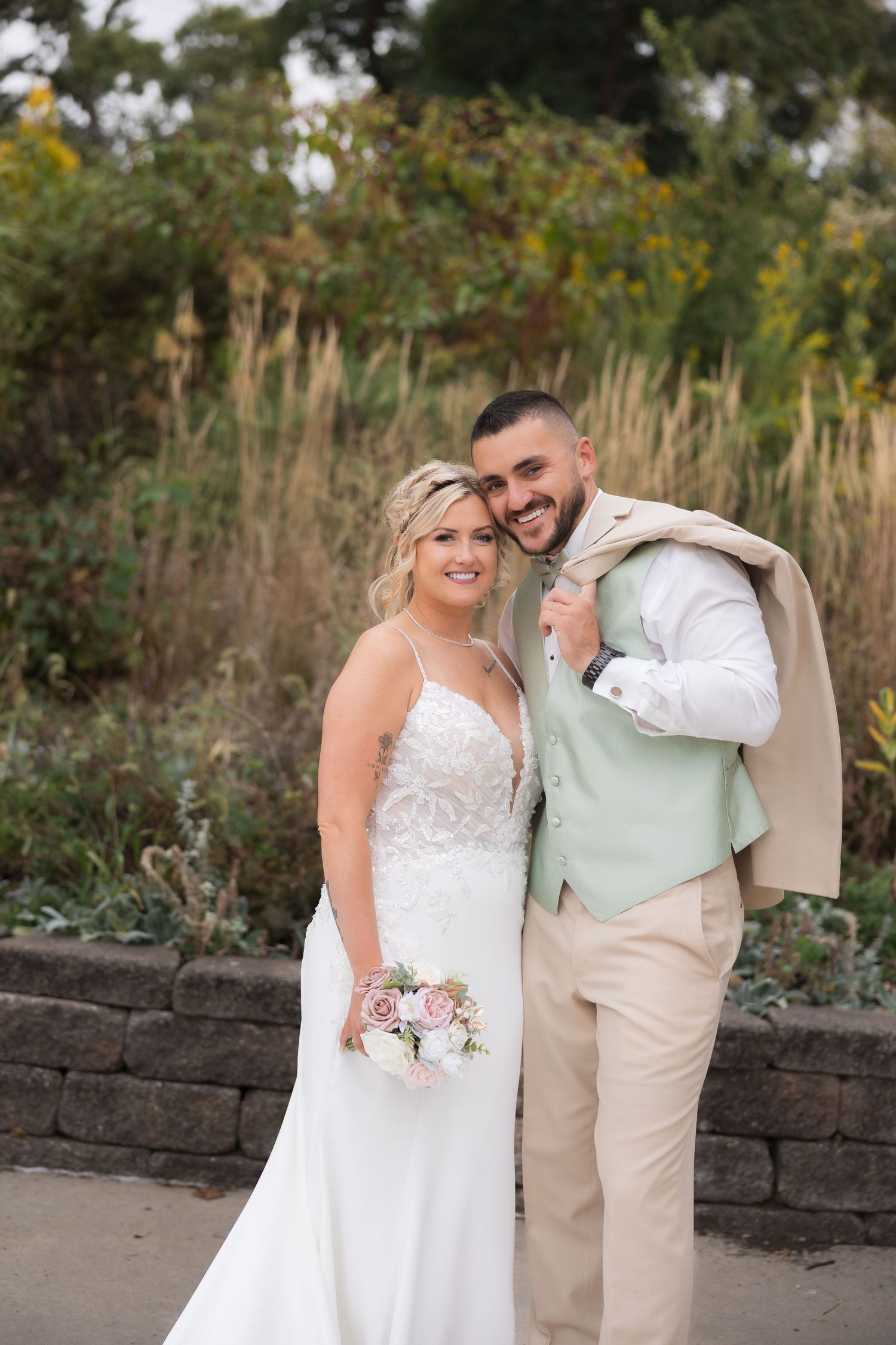 Romantic outdoor wedding portrait with couple embracing against natural foliage backdrop.