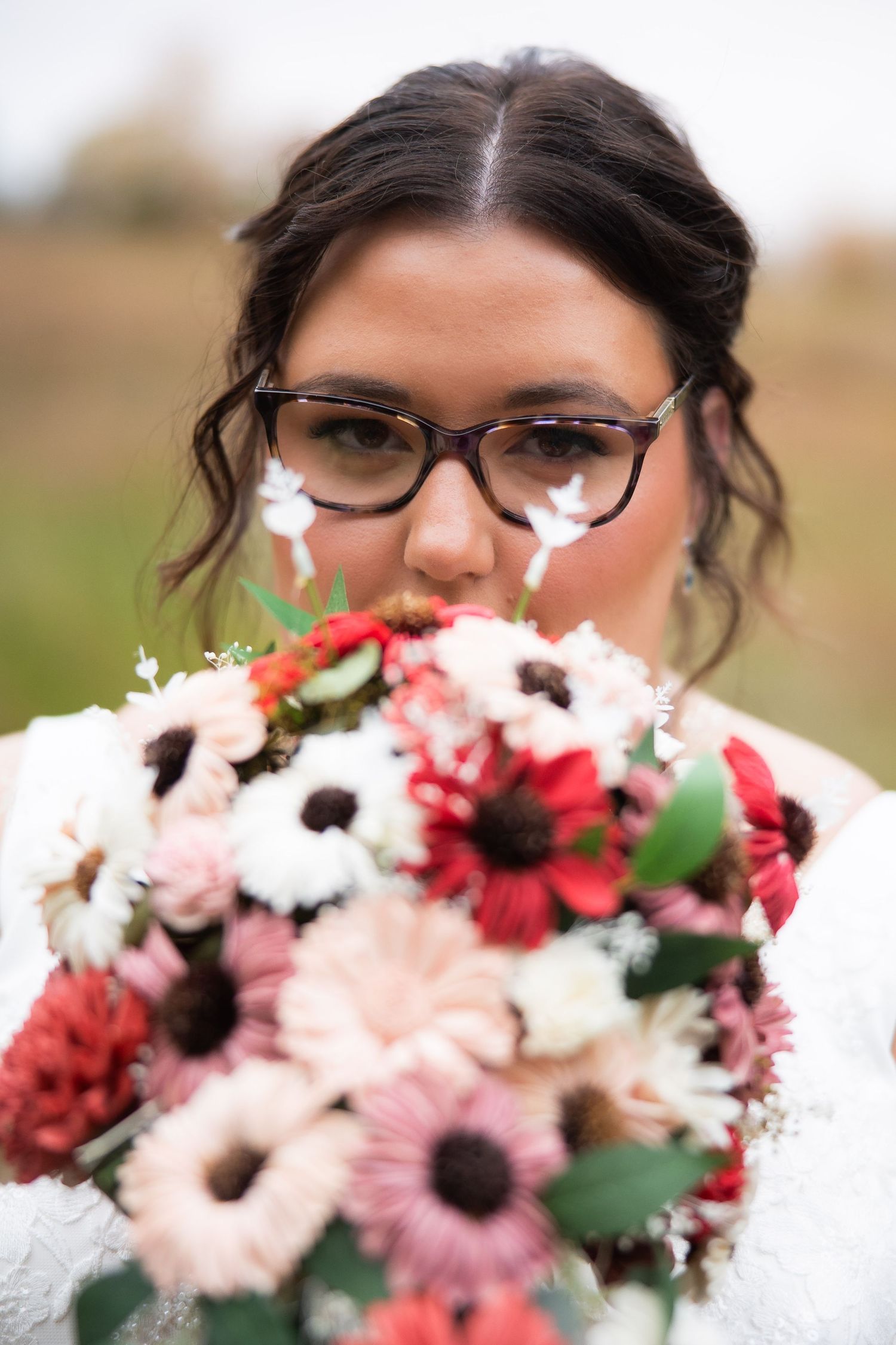 A close-up view of pink and red floral bouquets with daisies and greenery against a blurred outdoor background.